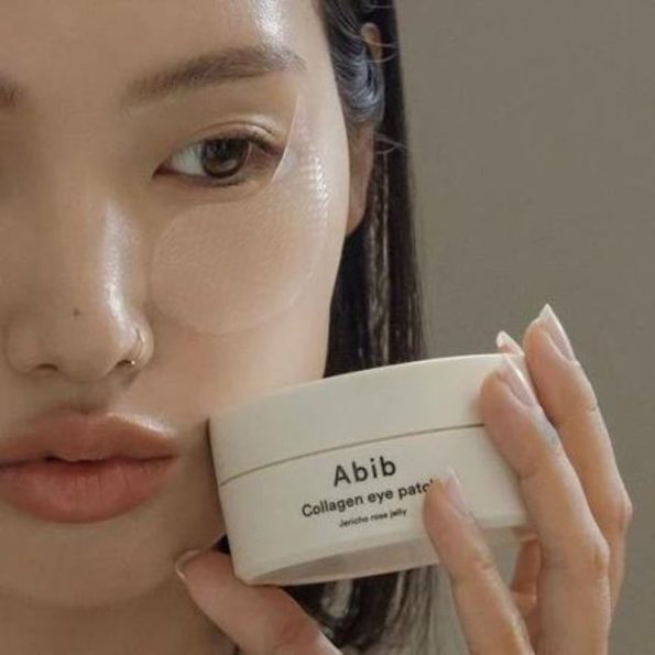 A woman applies Abib Collagen Eye Patch cream from a jar, enhancing her skincare routine with focused care for her face. | Korean Beauty Products NZ